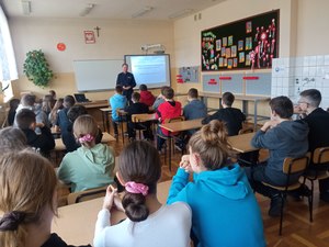 Policjant na zajęciach z uczniami w szkole w trakcie prowadzenia działań profilaktycznych.