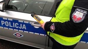 Policjant stoi przy radiowozie a w ręce trzyma alco sensor