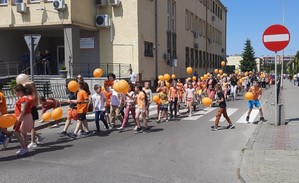 Dzieci podczas marszu przeciwko przemocy trzymają w dłoni pomarańczowe baloniki