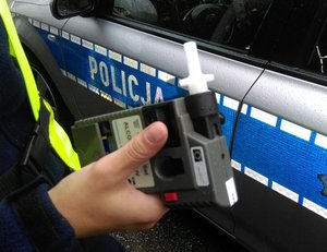 Policja stoi przy radiowozie i trzyma w ręce alkosensor