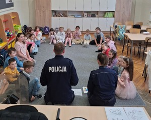 Policjanci siedzią na dywanie a wkoło nich siedzą również dzieci