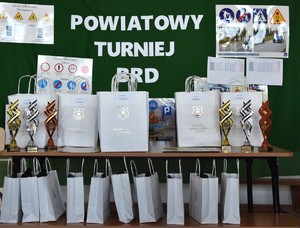Plakat z napisem Powiatowy Turniej BRD a puchary oraz  obok narody dla zwycięskich drużyn