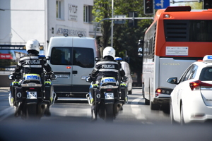 Na zdjęciu widać autobus i samochody osobowy i dwa policyjne motocykle które poruszają się ulicami miasta