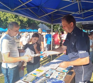 Dziec, młodzież i osoby starsze przy stoisku profilaktycznym oraz radiowozie policyjnym