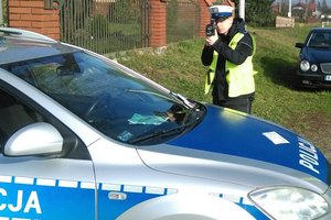 Policjant z  miernikiem prędkości stoi koło radiowozu