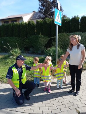 Policjant pokazuje dzieciom jak bezpiecznie przejść przez jezdnię