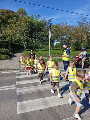 Policjant pokazuje dzieciom jak bezpiecznie przejść przez jezdnię