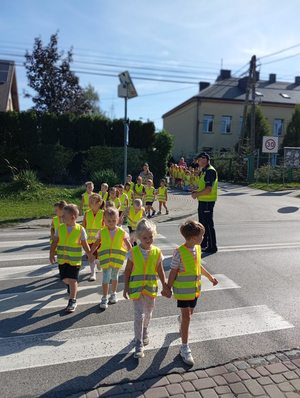 Policjant pokazuje dzieciom jak bezpiecznie przejść przez jezdnię