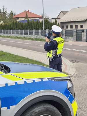 Policjantka przeworskiej drogówki, stojąca obok radiowozu, mierzy prędkość.